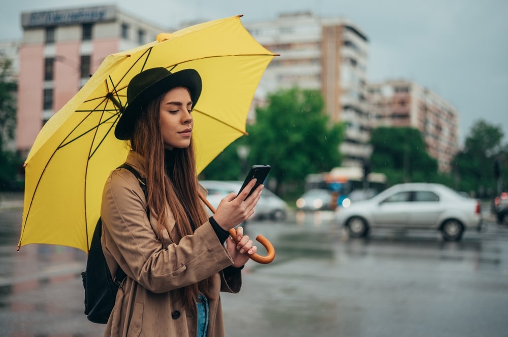žena drži mobitel u rukama i nosi žuti kišobran dok proučava upoznavanje preko interneta