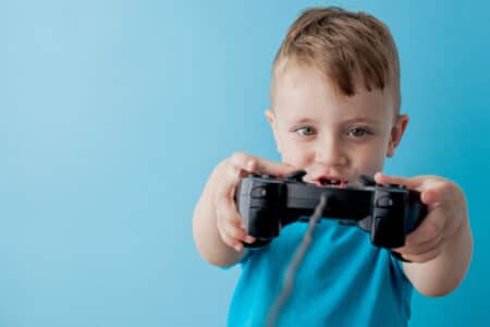 Slika prikazuje dijete koje drži konzolu dok igra video igrice za djecu do 5 godina.